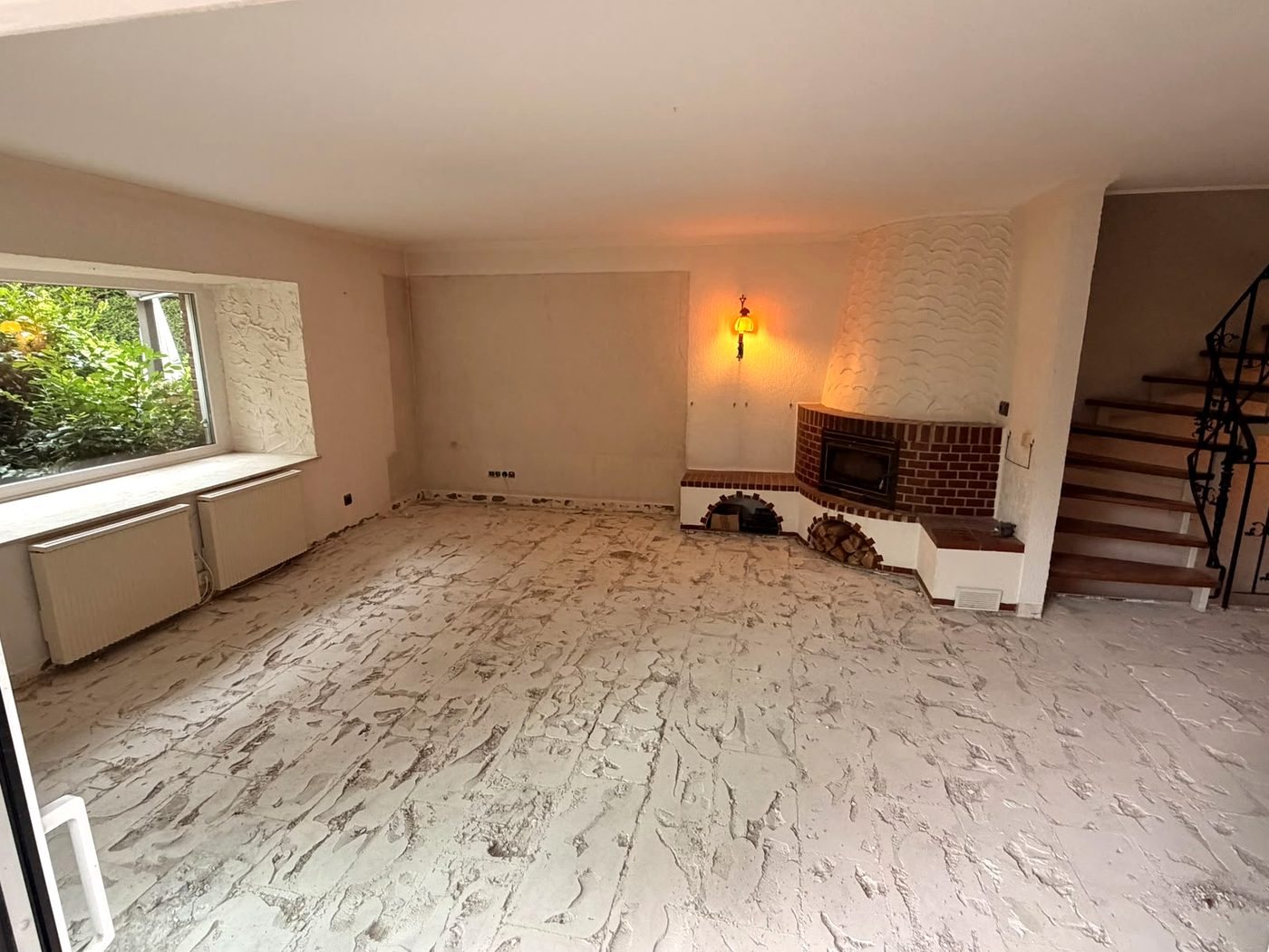 Wohnzimmer nach dem Rückbau: Bodenfliesen entfernt, Kamin und Treppe stehen