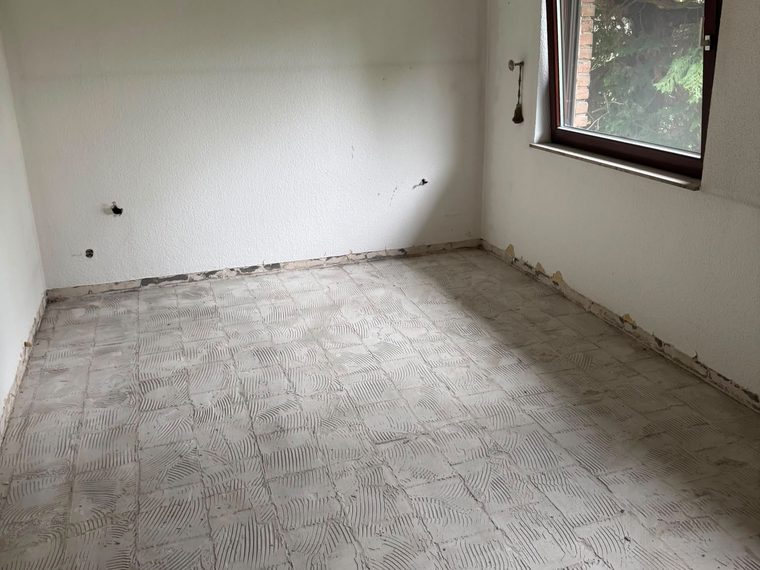 Zimmer im Erdgeschoss nach dem Rückbau, Bodenfliesen entfernt, Kleberbett liegt frei